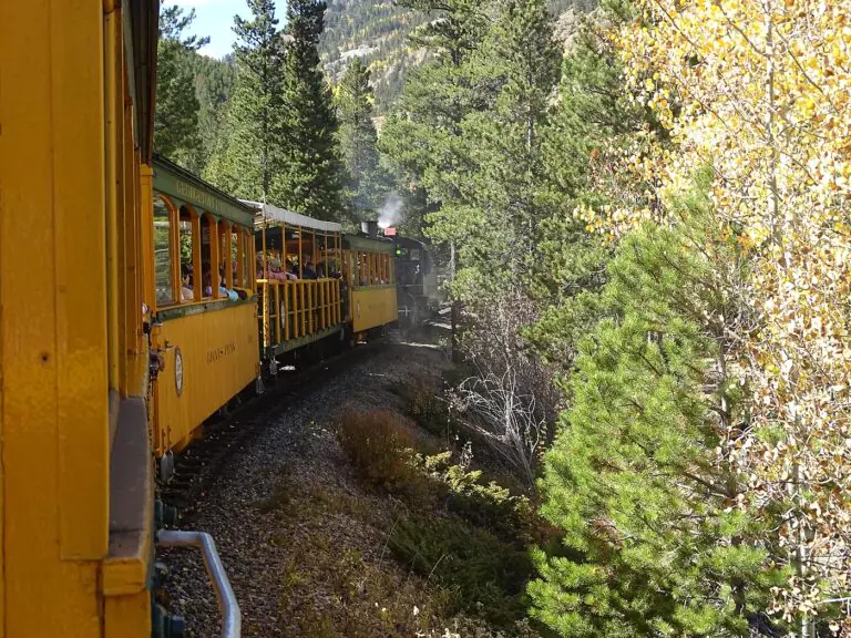 Yellow Georgetown Loop Railroad cars curving through pines and autumn aspens behind a steam locomotive